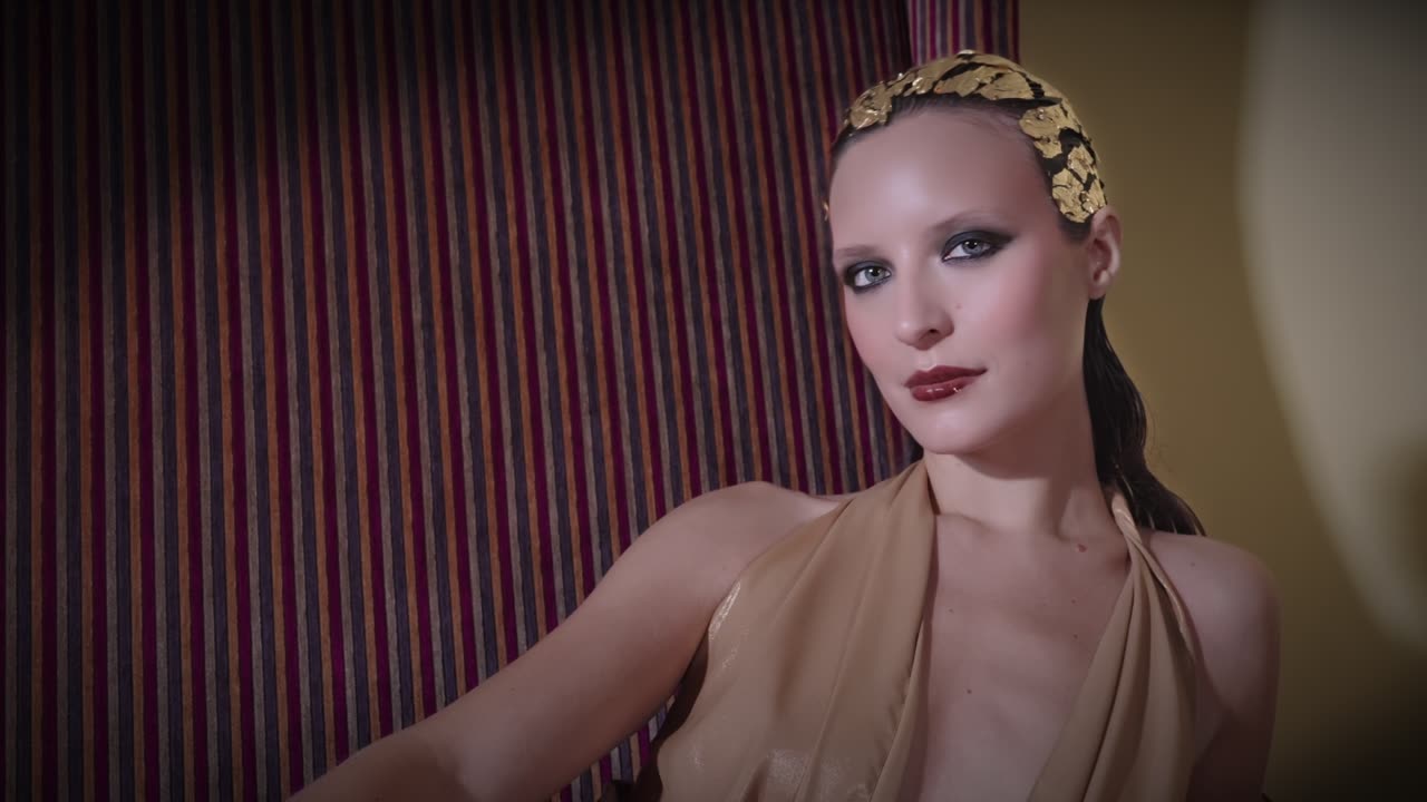 Una modella con una corona di foglie d’oro e un abito color sabbia, su un divano a righe