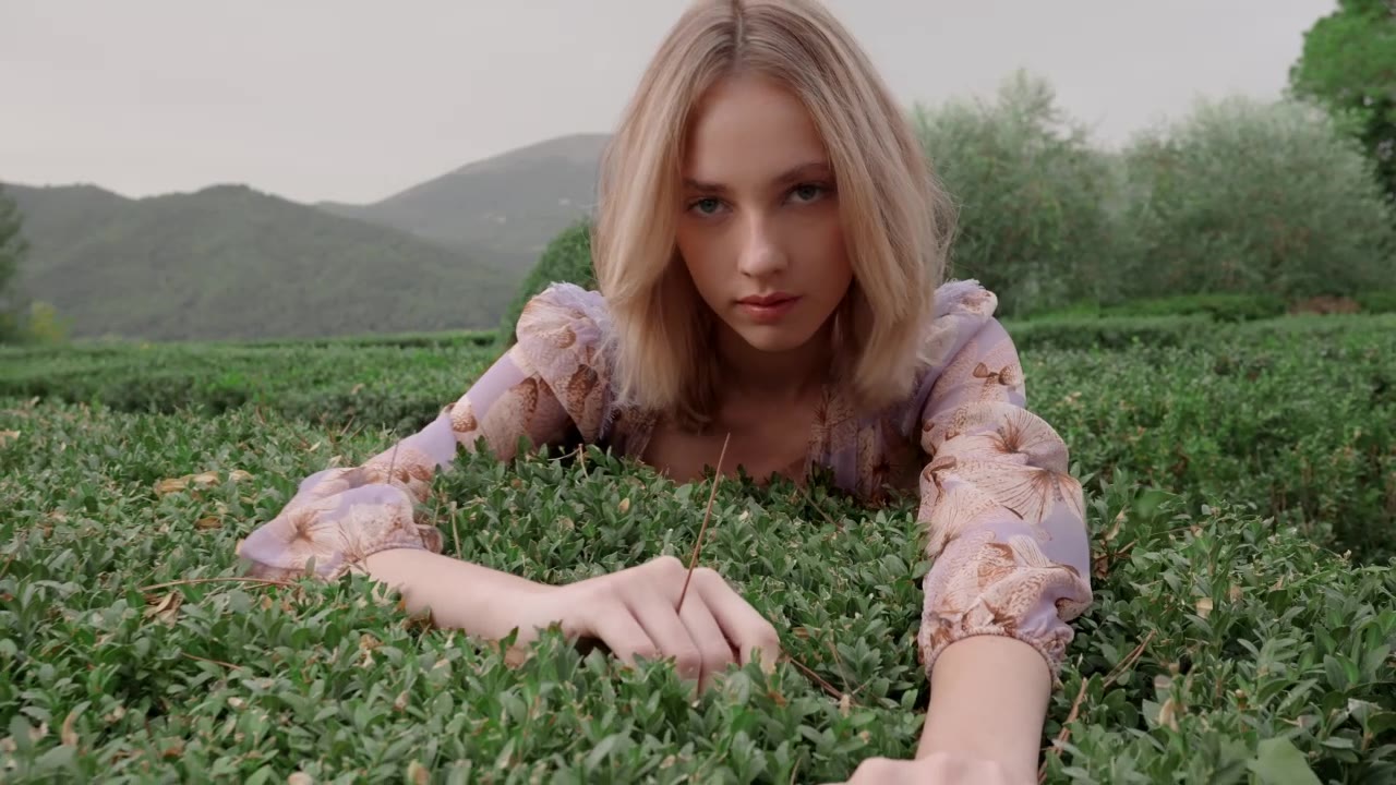 Una modella bionda distesa su una siepe di bosso, con le colline sullo sfondo