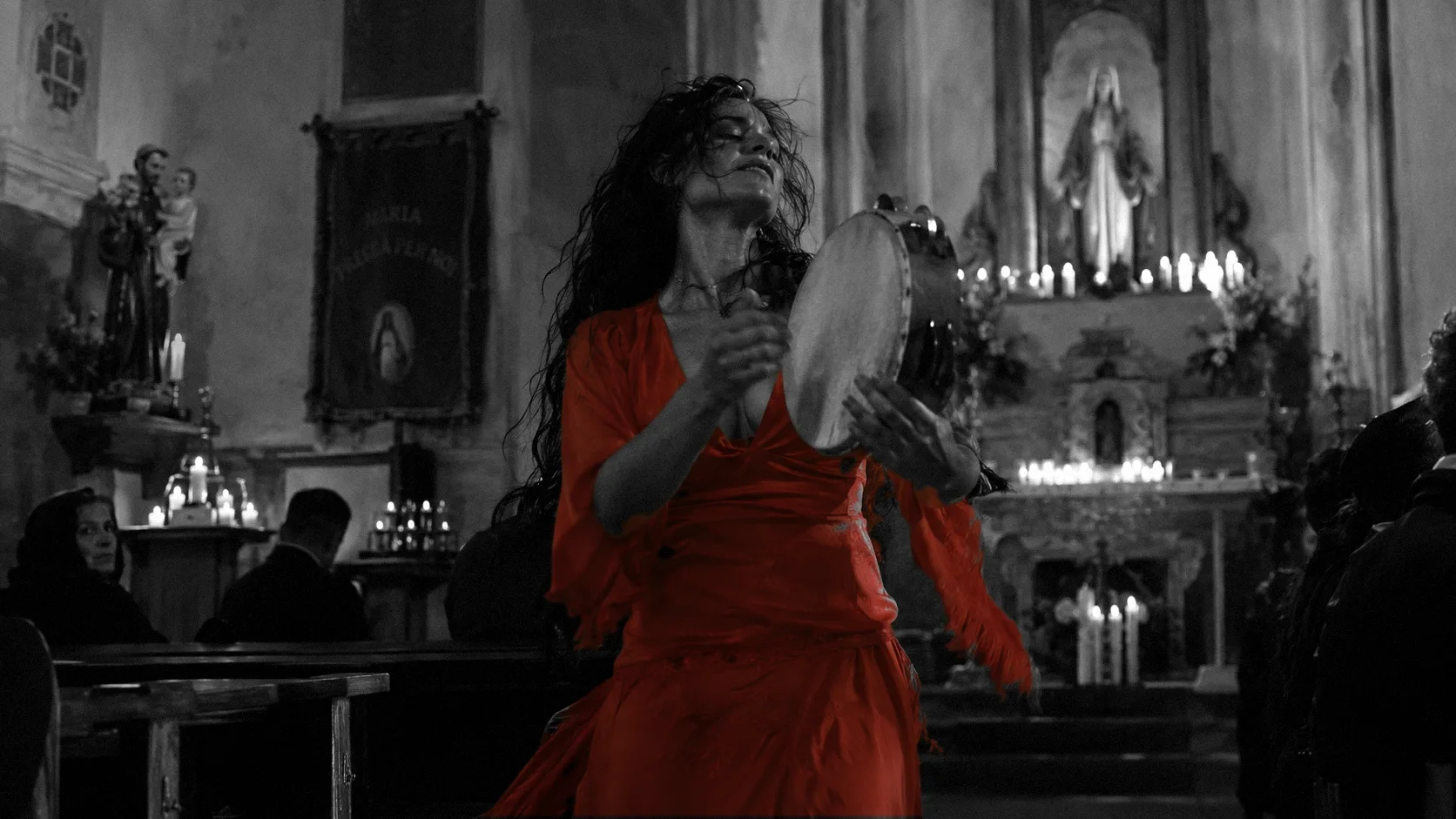 Una donna in abito rosso suona il tamburello e canta in una chiesa di paese, davanti all’altare